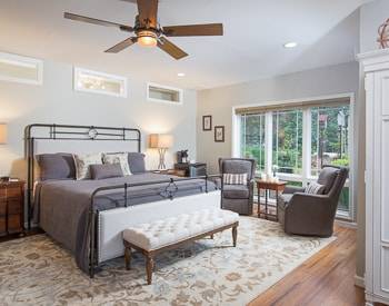 Grey rod iron bed frame with fabric inlay, two grey high back chairs with a view of the mountains, flora carpet on light wood floors